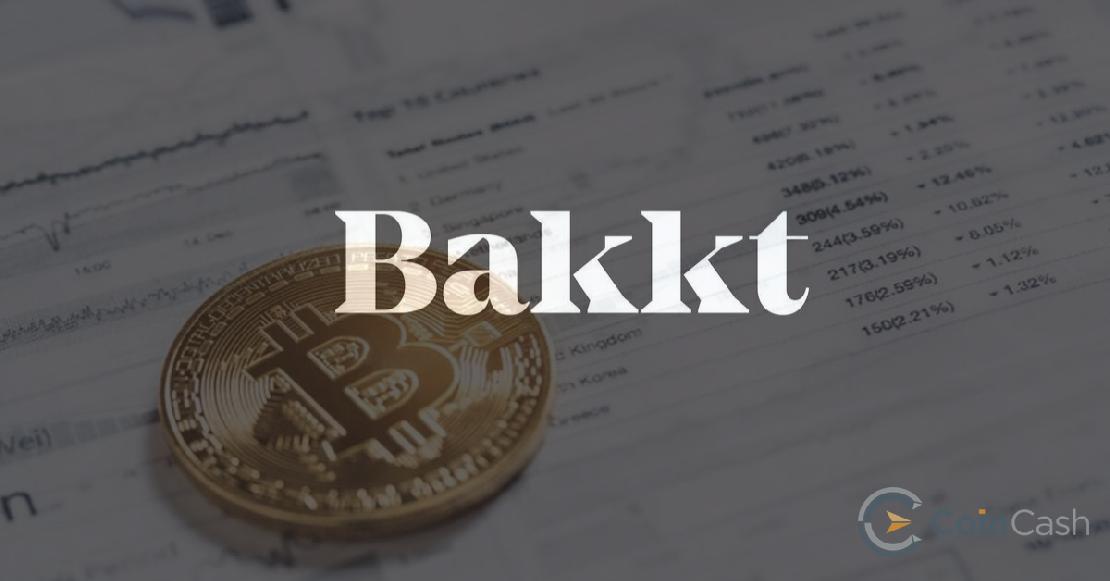 Bakkt logó, a háttérben pedig bitcoin érmék egy papíron.